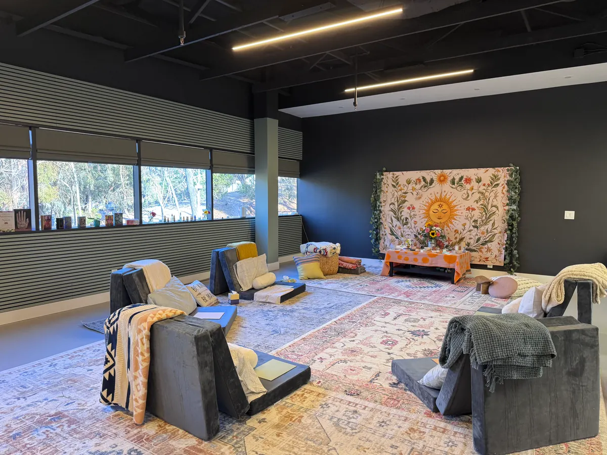 The room set for a retreat — floor seats and blankets on layered rugs, and a floral sun tapestry above a low altar table.